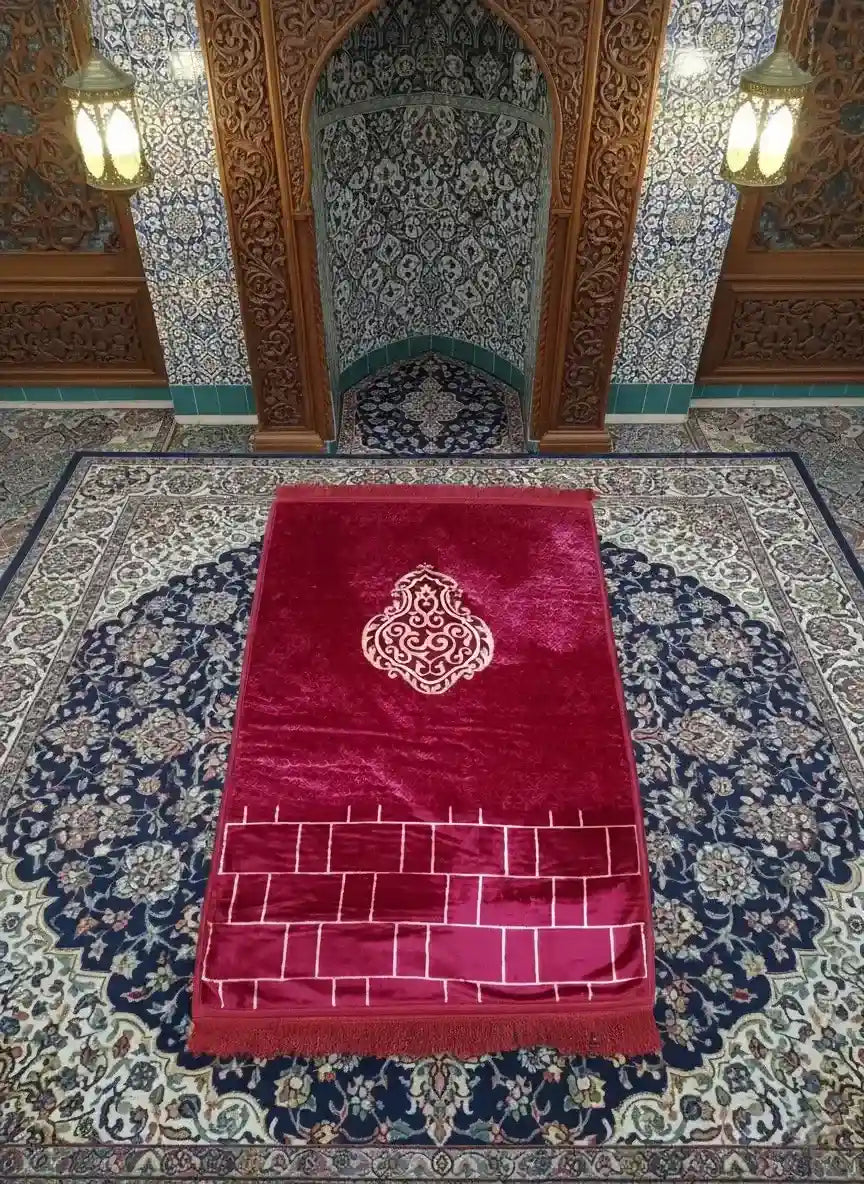 Red prayer mat with intricate design on a patterned floor in a mosque.